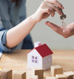 close-up-woman-s-hand-giving-house-key-man-wooden-table