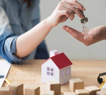 close-up-woman-s-hand-giving-house-key-man-wooden-table